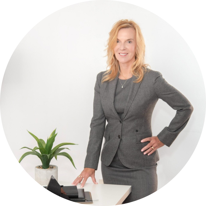 A woman in grey suit standing next to plant.